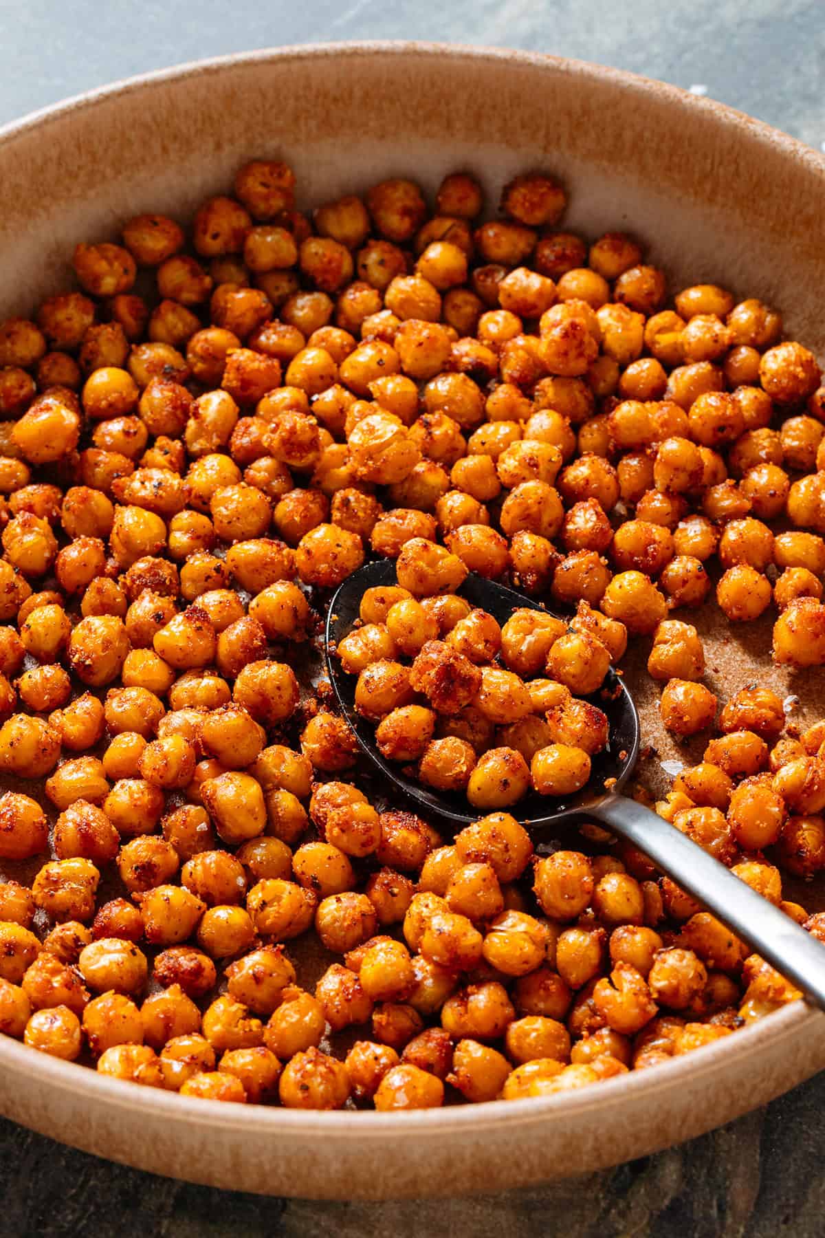 Golden roasted chickpeas with spices in a brown low bowl and a spoon in the bowl.