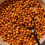 Golden roasted chickpeas with spices in a brown low bowl and a spoon in the bowl.