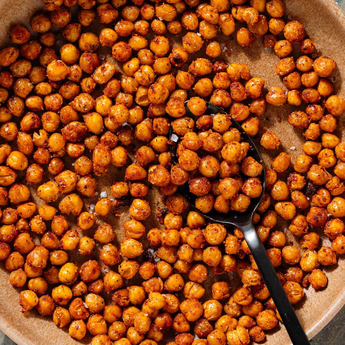 Golden roasted chickpeas with spices in a brown low bowl and a spoon in the bowl.