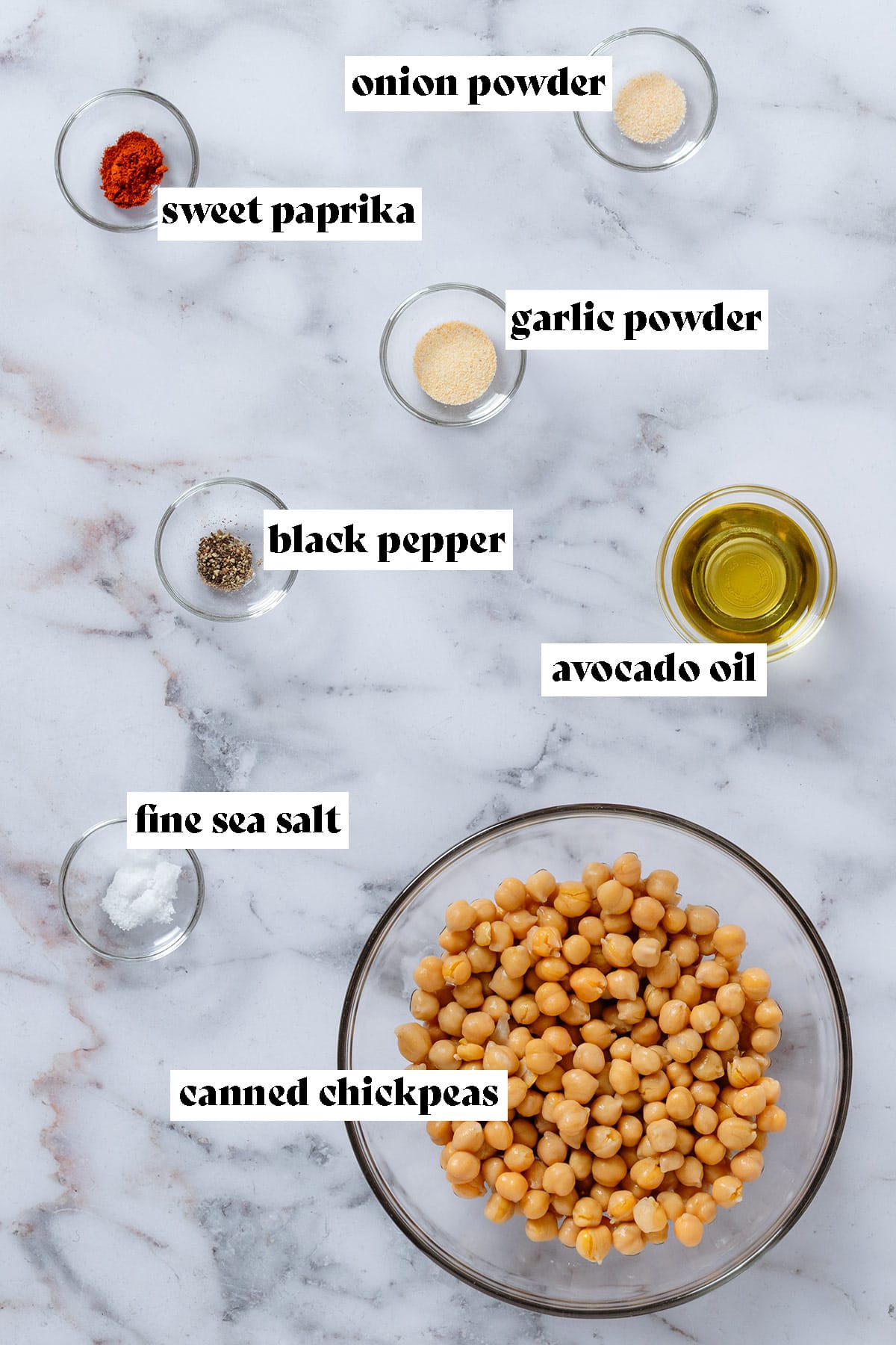 Glass bowls with ingredients like canned chickpeas, avocado oil, garlic powder, onion powder, and other spices.