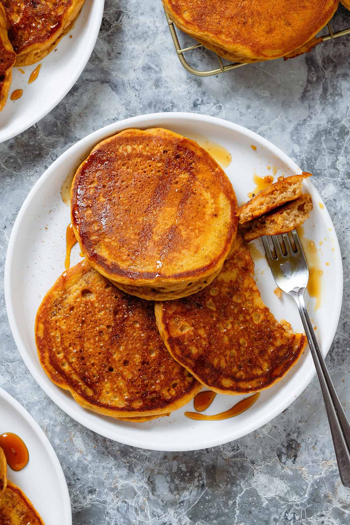 A white plate with three sweet potato pancakes and a light drizzle of maple syrup with a bite on a fork.