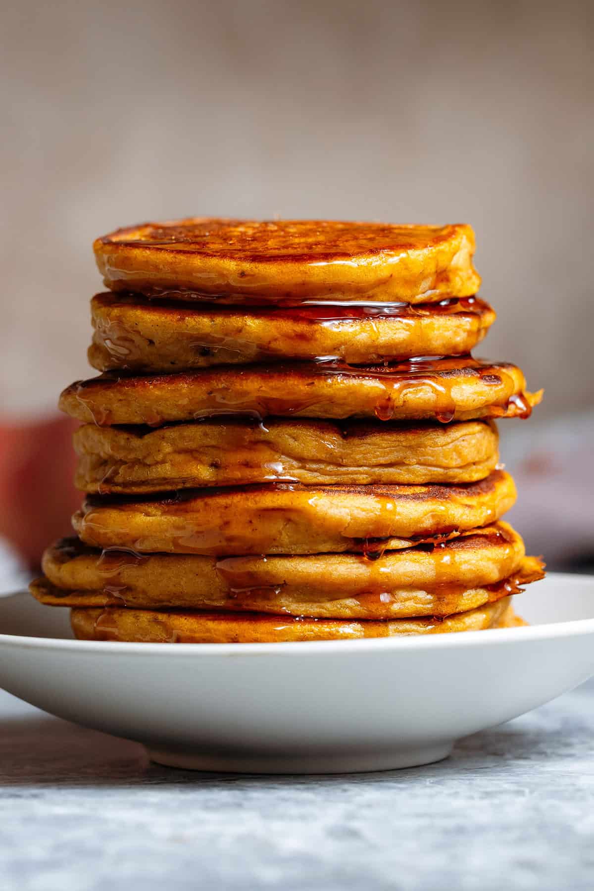 A stack of sweet potato pancakes drizzled with maple syrup on a small white plate.