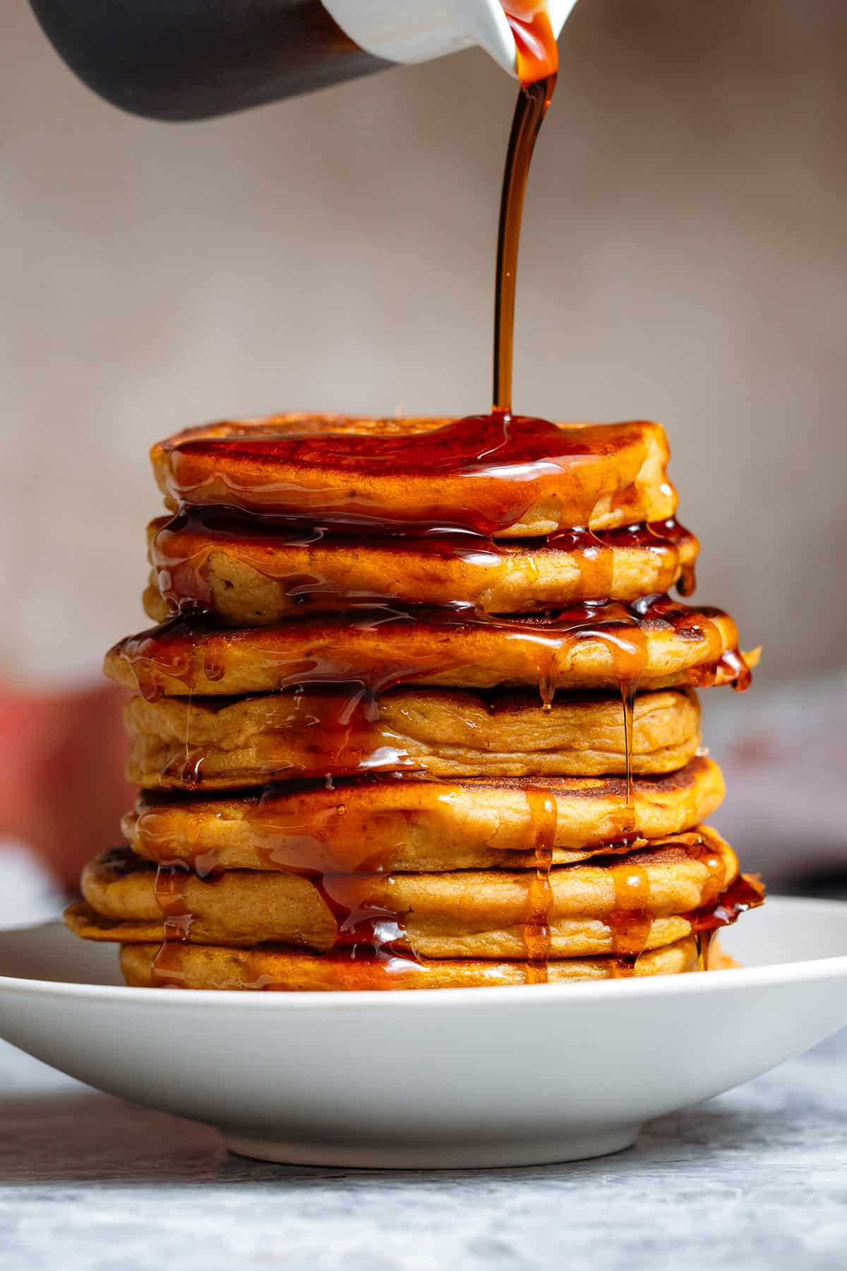 A stack of sweet potato pancakes being drizzled with maple syrup on a small white plate.