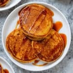 Three pancakes on a white plate with a light drizzle of maple syrup and a dusting of cinnamon.
