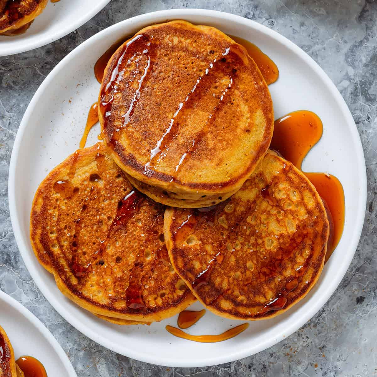 Three pancakes on a white plate with a light drizzle of maple syrup and a dusting of cinnamon.
