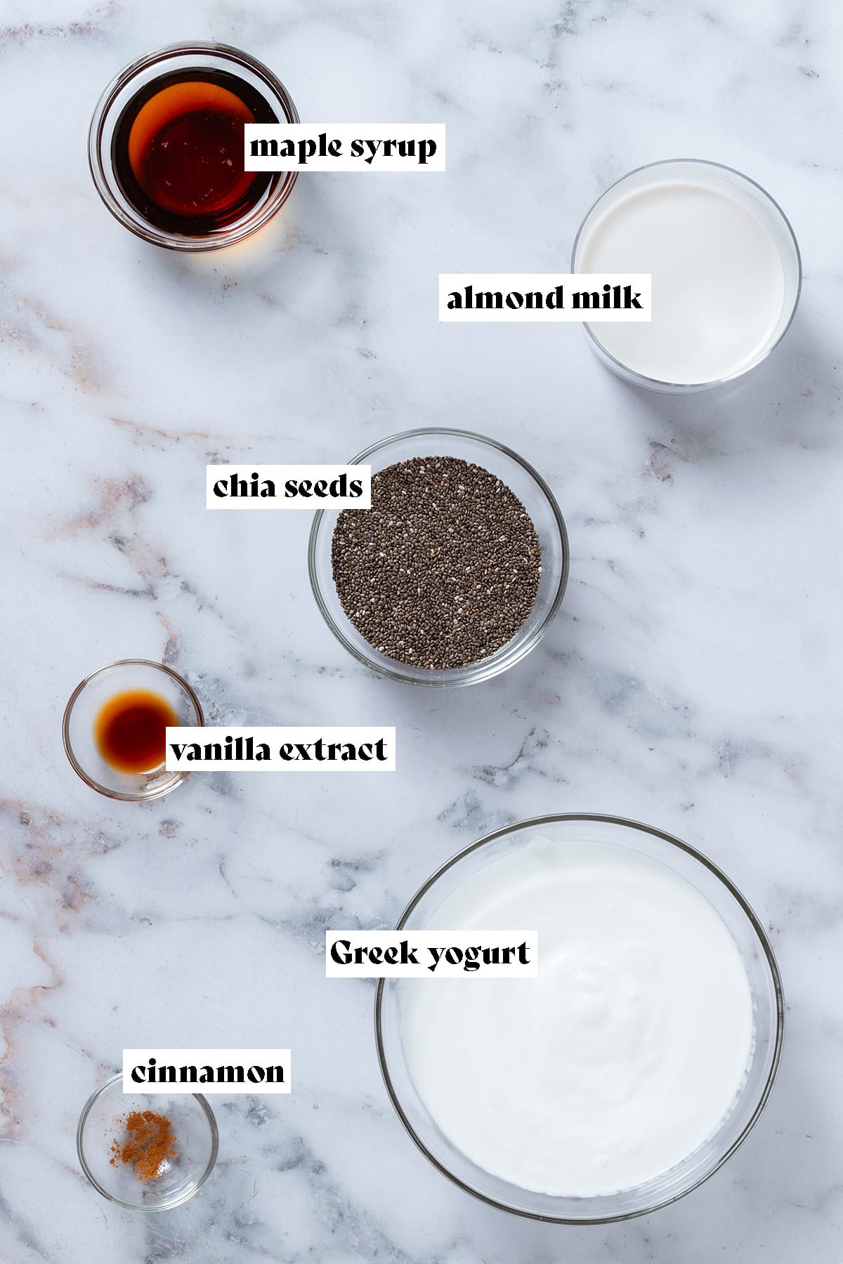 Small bowls with ingredients like chia seeds, almond milk, Greek yogurt, maple syrup, and spices with text overlay.
