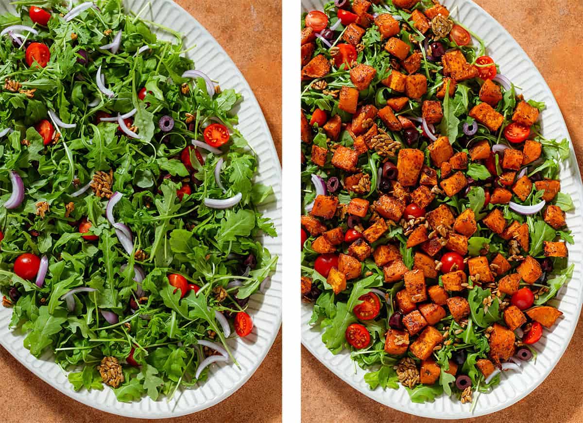 A large serving plate with arugula, cherry tomatoes, red onion, olives, and roasted sunflower seeds on the left and topped with roasted sweet potatoes on the right.