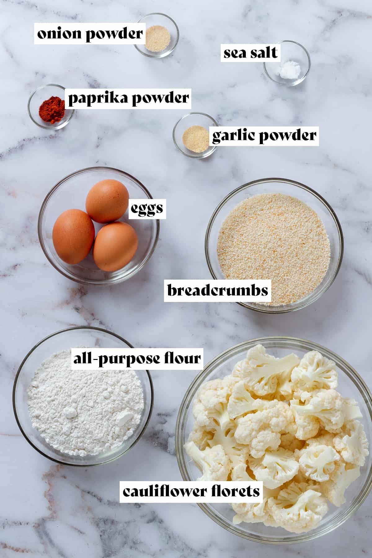 Glass bowls with ingredients like eggs, flour, cauliflower florets, breadcrumbs, and spices on a marble background with text overlay.
