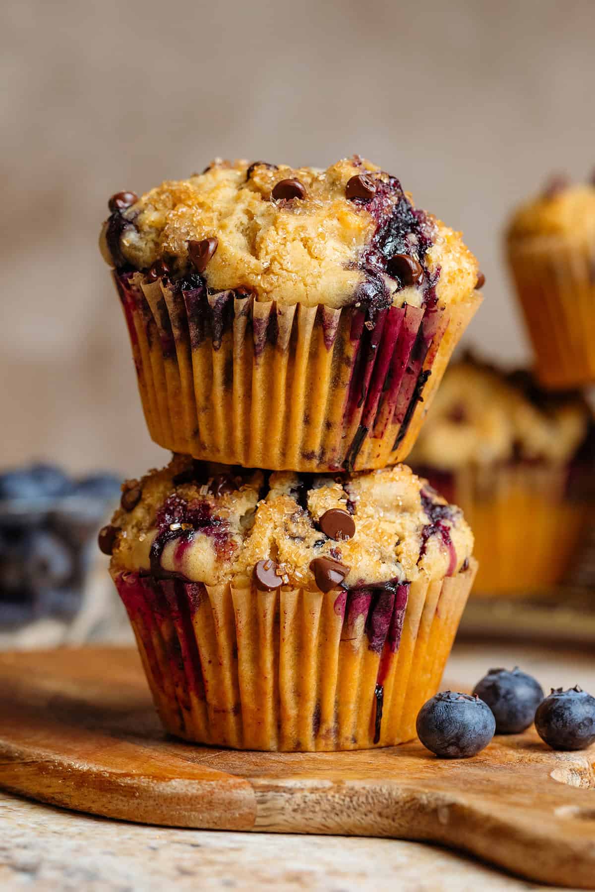 Two blueberry chocolate chip muffins stacked on a small wooden cutting board.