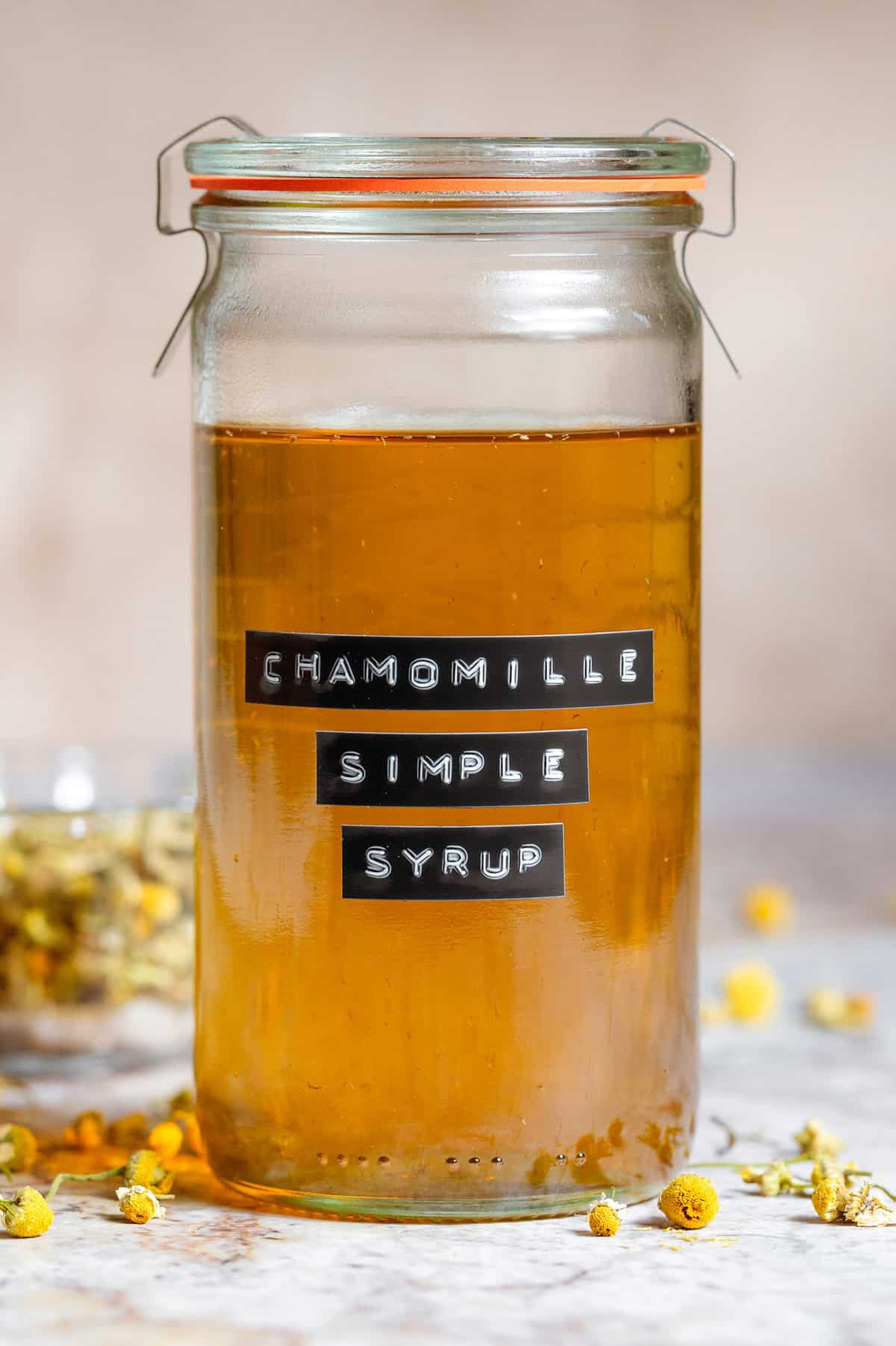 Golden chamomile simple syrup in a tall glass jar with an embossed label.