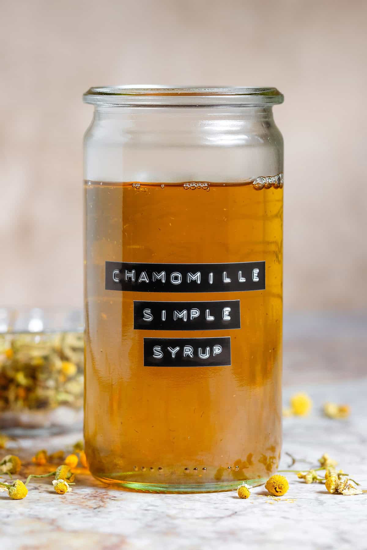 Golden chamomile simple syrup in a tall glass jar with an embossed label without a lid.