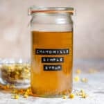 Golden chamomile simple syrup in a tall glass jar with an embossed label.