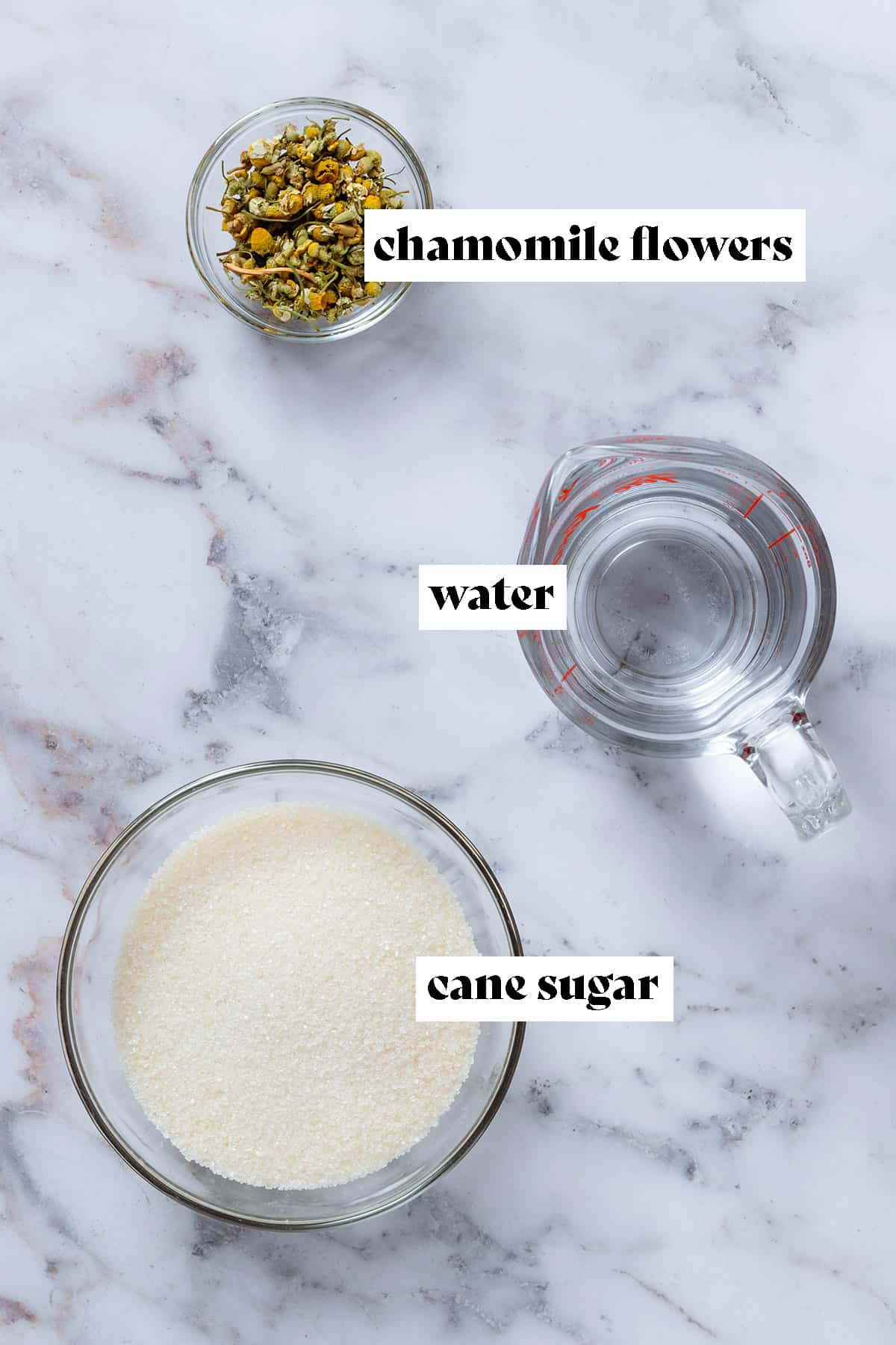 Cane sugar in a bowl, water in a measuring cup, and dried chamomile flowers in a small bowl.