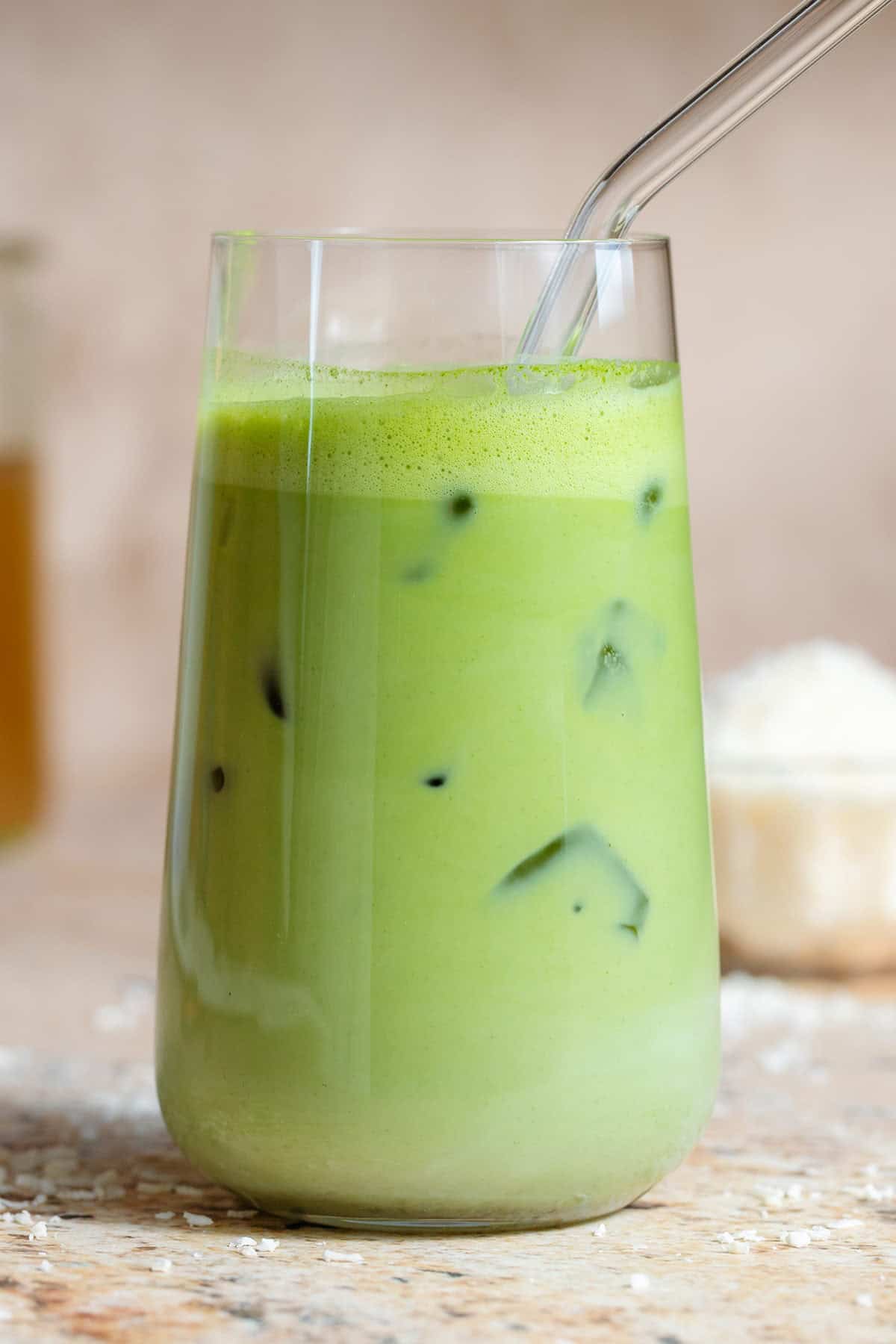 Iced matcha latte in a tall glass with a glass straw and shredded coconut in the background.