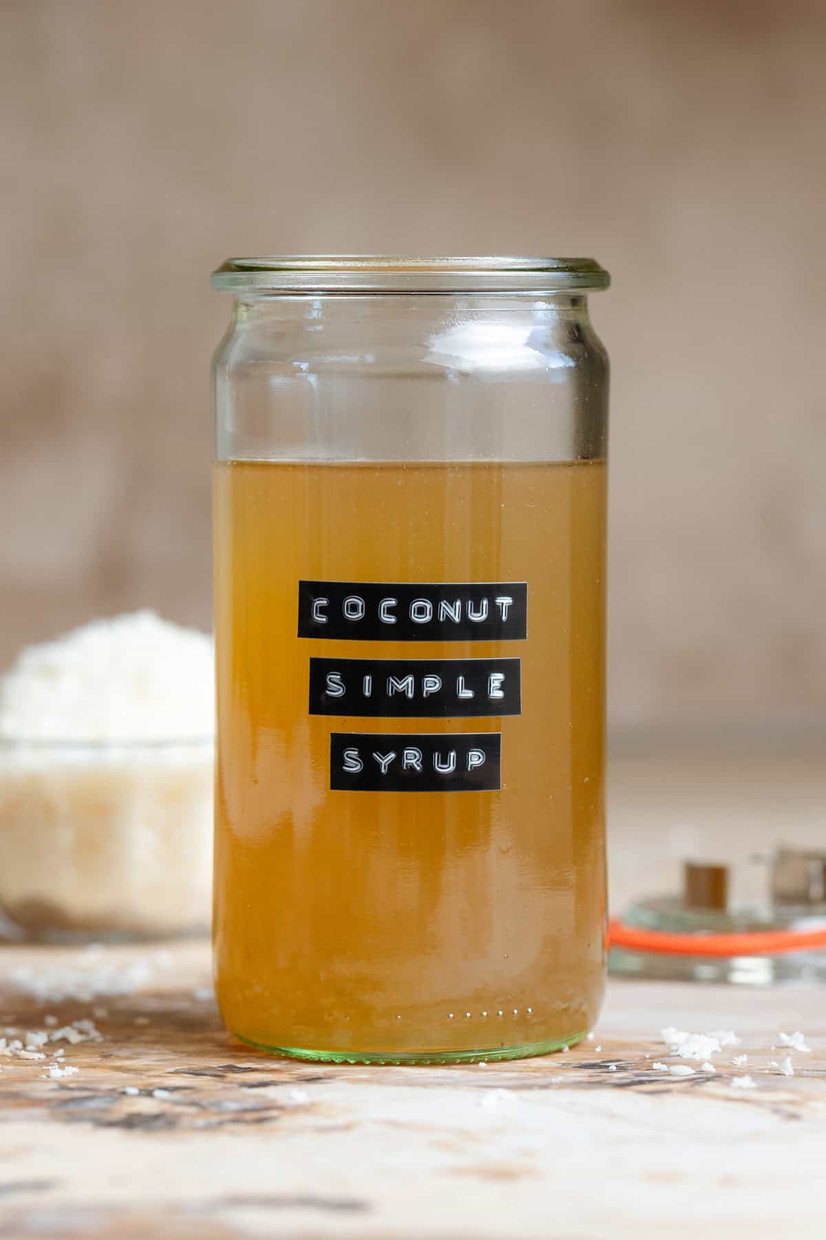 Coconut simple syrup in a tall glass jar without a lid with a black embossed label.