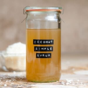 Coconut simple syrup in a tall glass jar with a black embossed label.