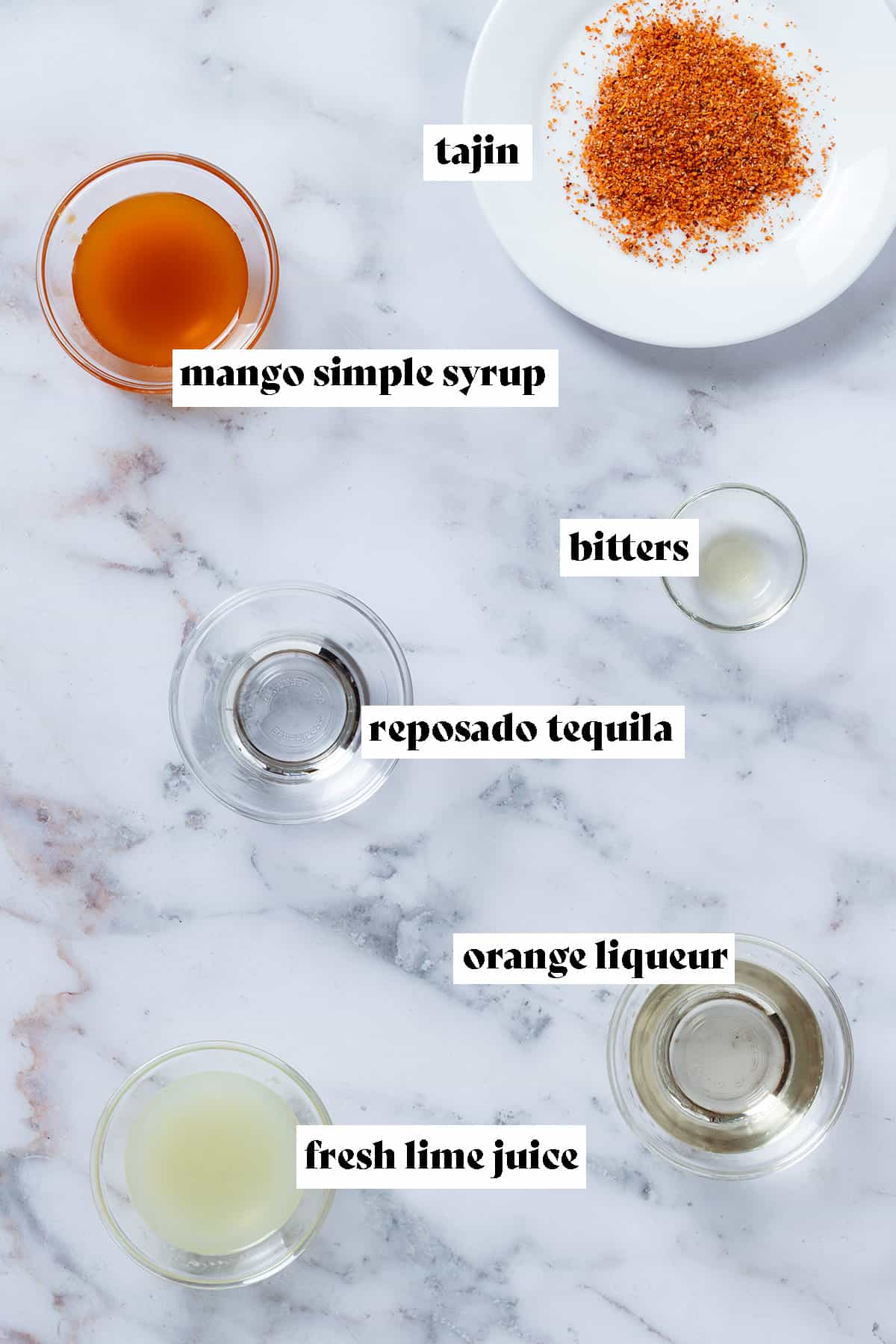 Tajin on a small white plate and cocktail in gredients like tequila, lime juice, mango syrup, and bitters in small glass bowls with text overlay.