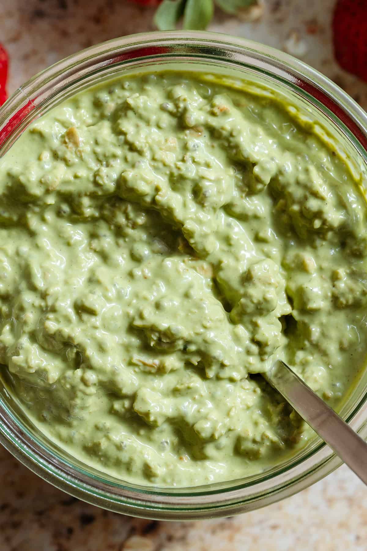 Creamy matcha overnight oats in a glass jar with a spoon on the right.