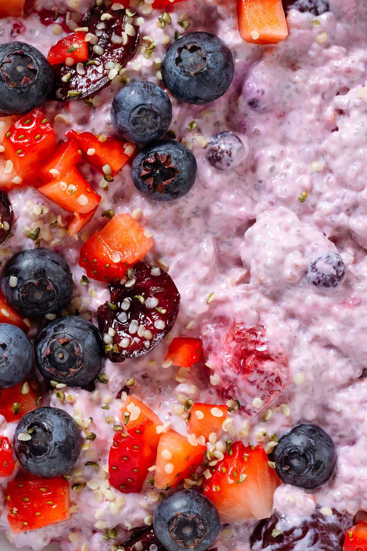 Light purple chia pudding with mixed berries topped with fresh blueberries, cherries, and chopped strawberries, sprinkled with hemp hearts.