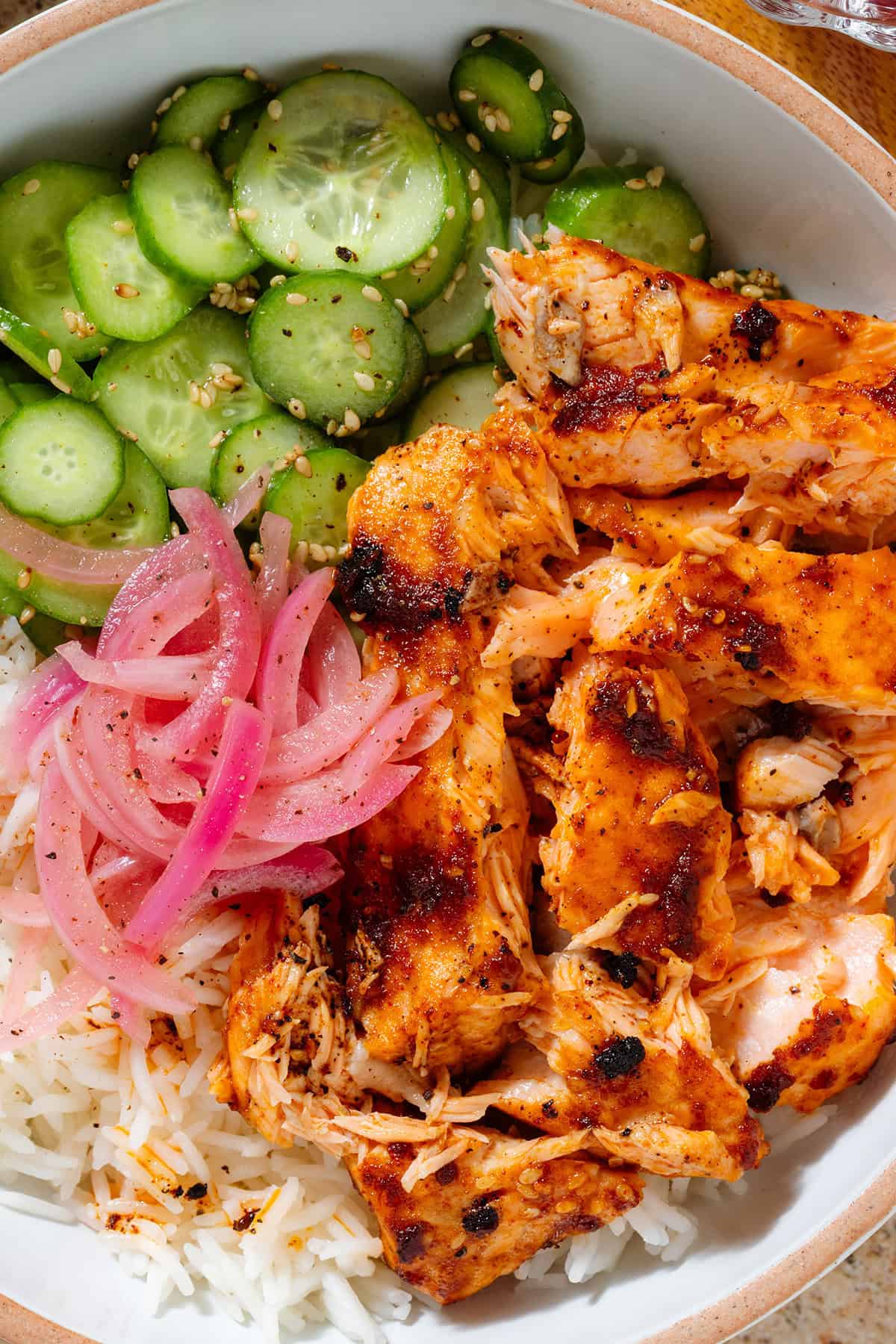 Chili crisp salmon rice bowl with sliced cucumber, sesame seeds, and pickled red onion.