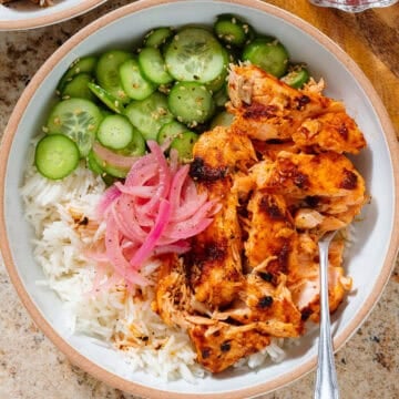 Chili crisp salmon rice bowl with sliced cucumber, sesame seeds, and pickled red onion.