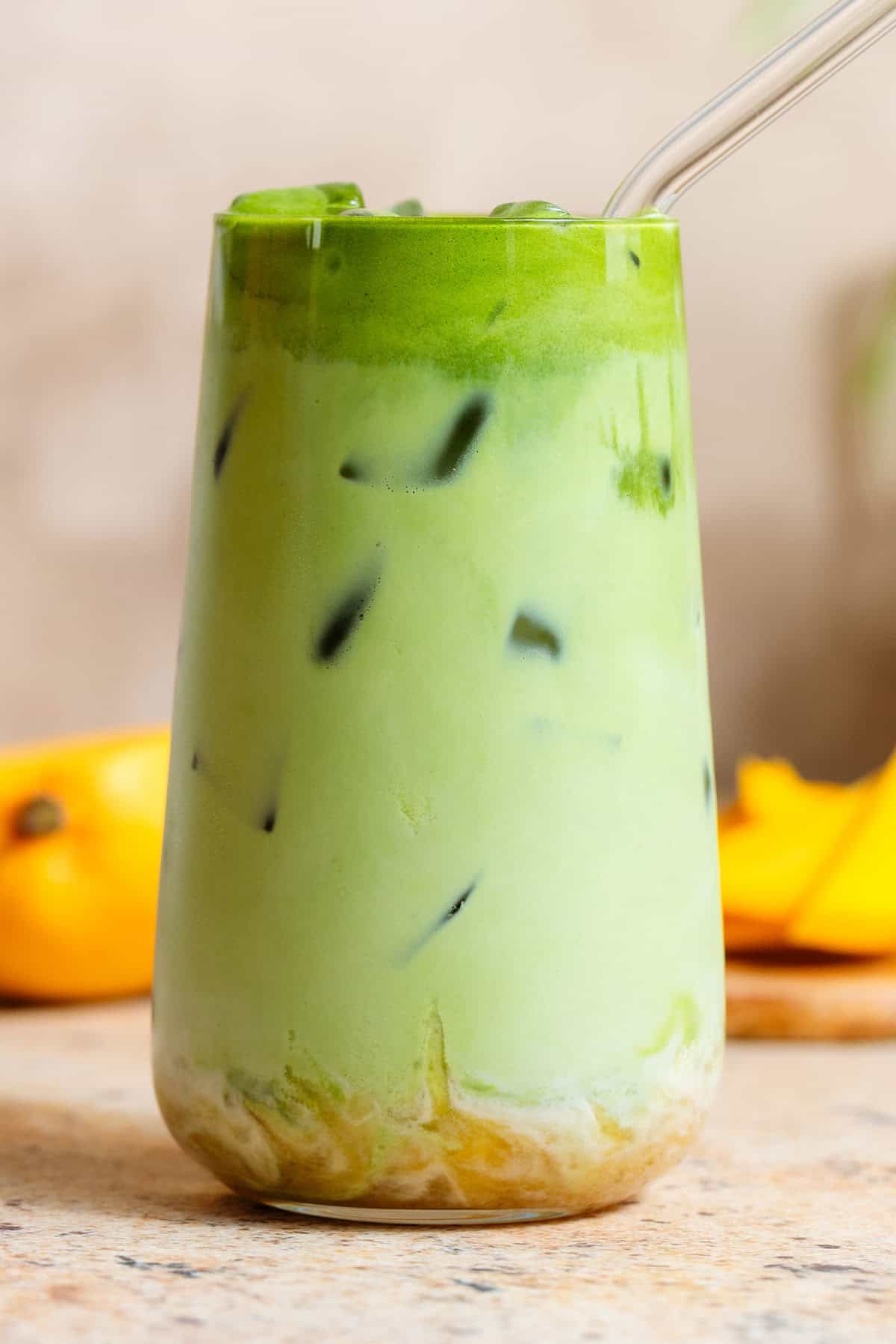 Bright green iced matcha latte in a tall glass with matcha syrup on the bottom, with a glass straw.