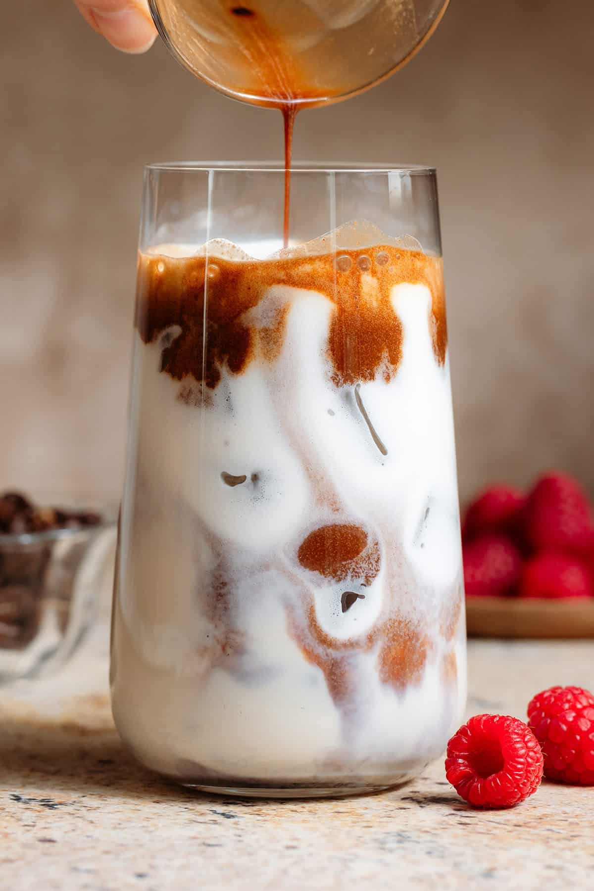 Espresso mixed with syrup being slowly poured over ice and milk in a tall glass.