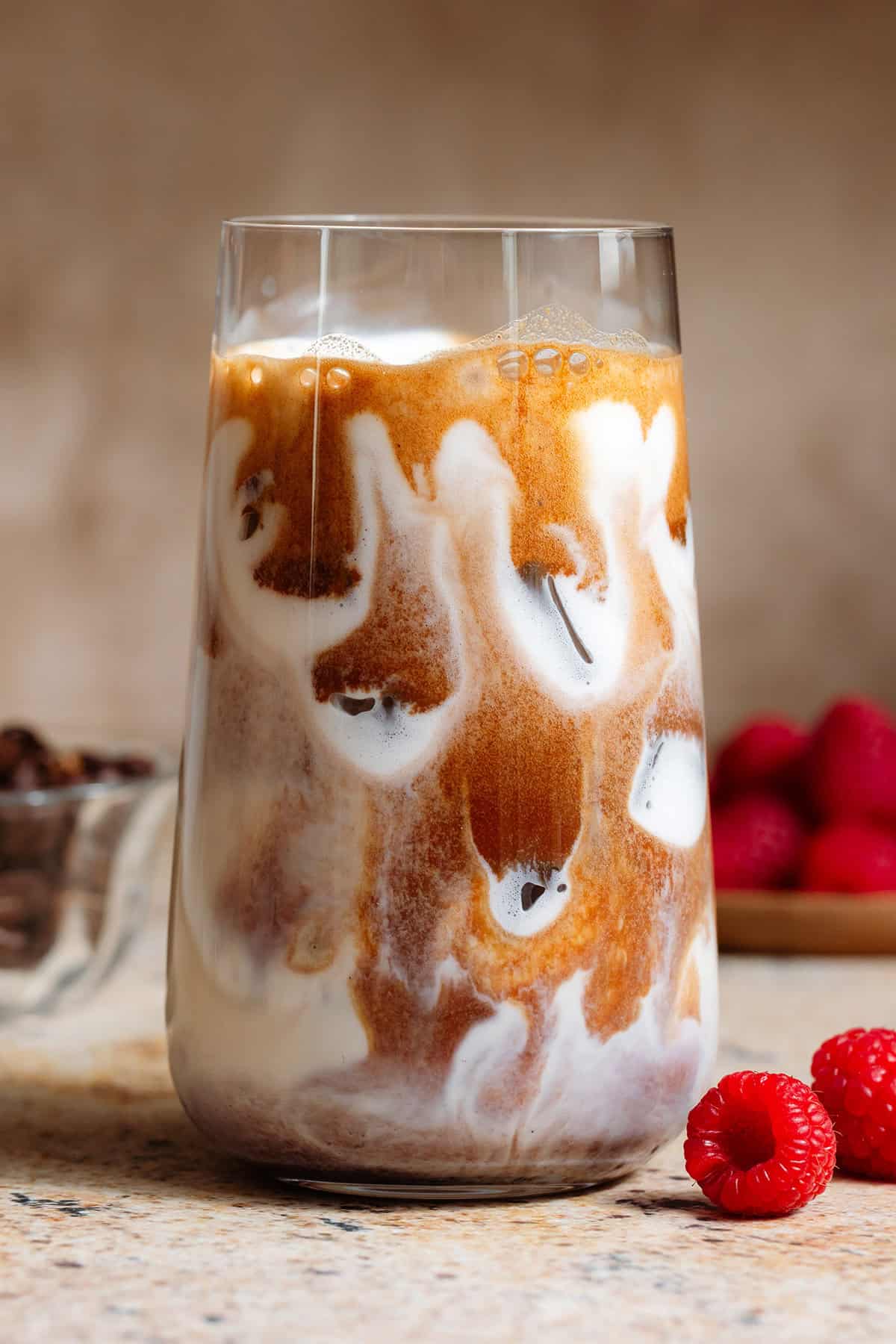 Espresso slowly mixing with milk in a tall glass filled with ice.