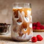 Espresso slowly mixing with milk in a tall glass filled with ice.