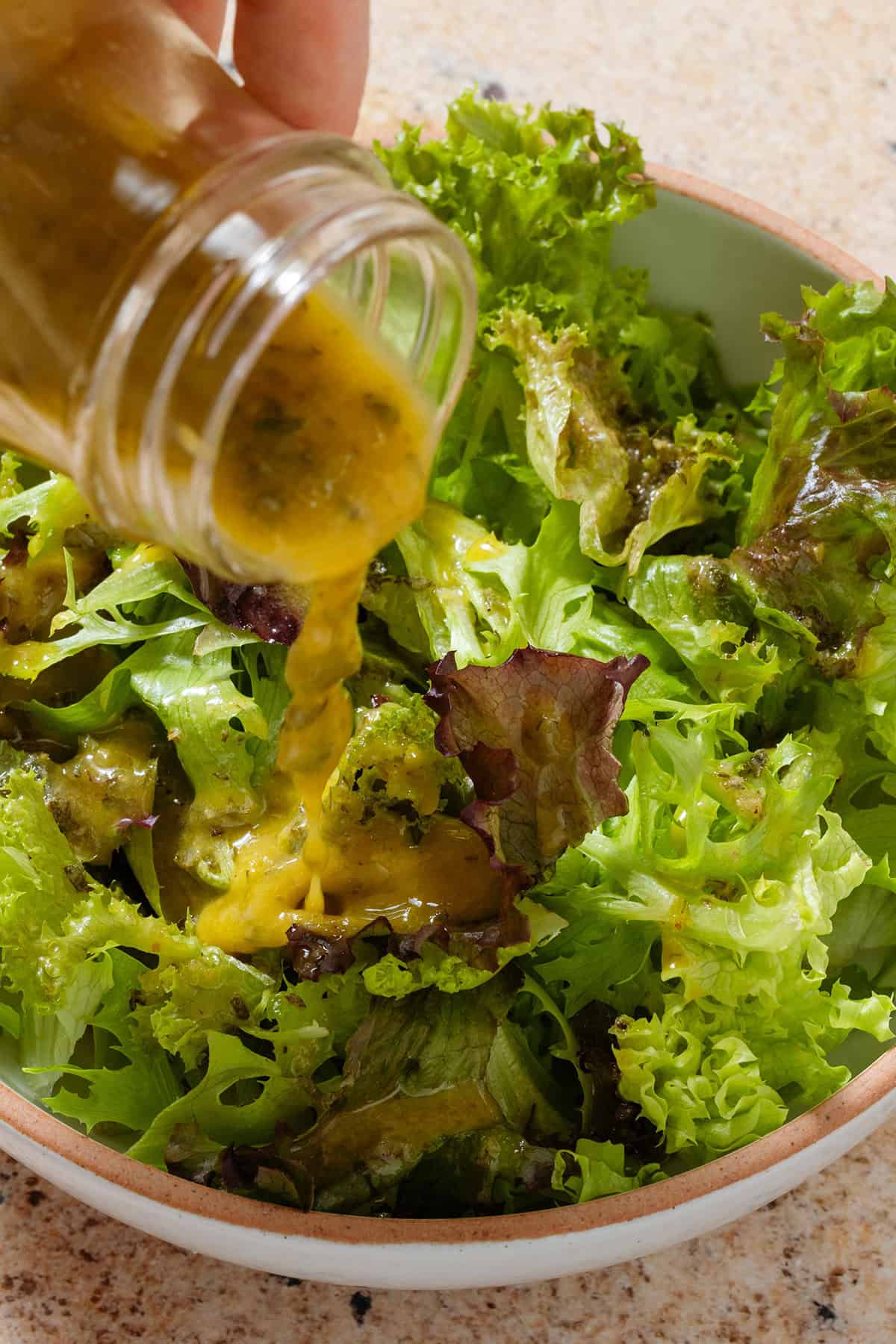 Vinaigrette being drizzled over mixed lettuce leaves in a bowl.
