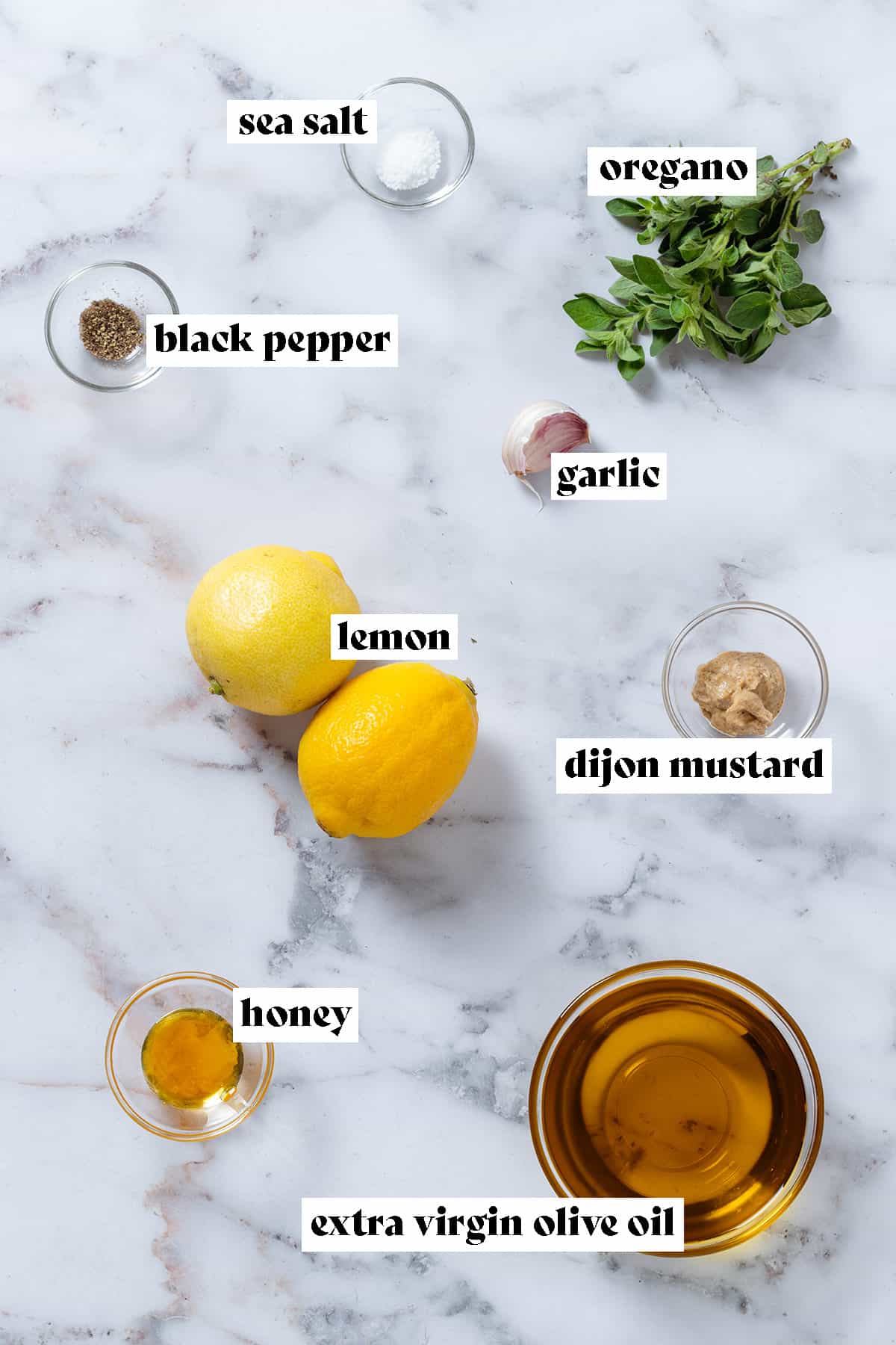 Olive oil, lemon, dijon mustard, oregano, and other ingredients in small glass bowls.