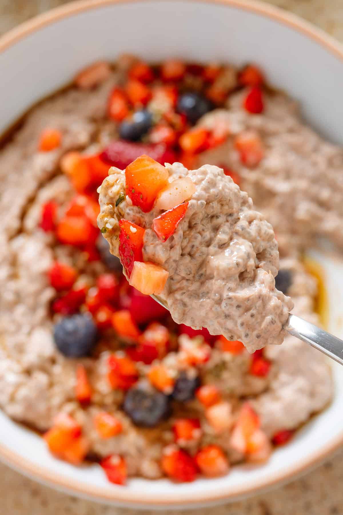 A spoon holding chocolate chia pudding with diced strawberries over a white bowl of the pudding.