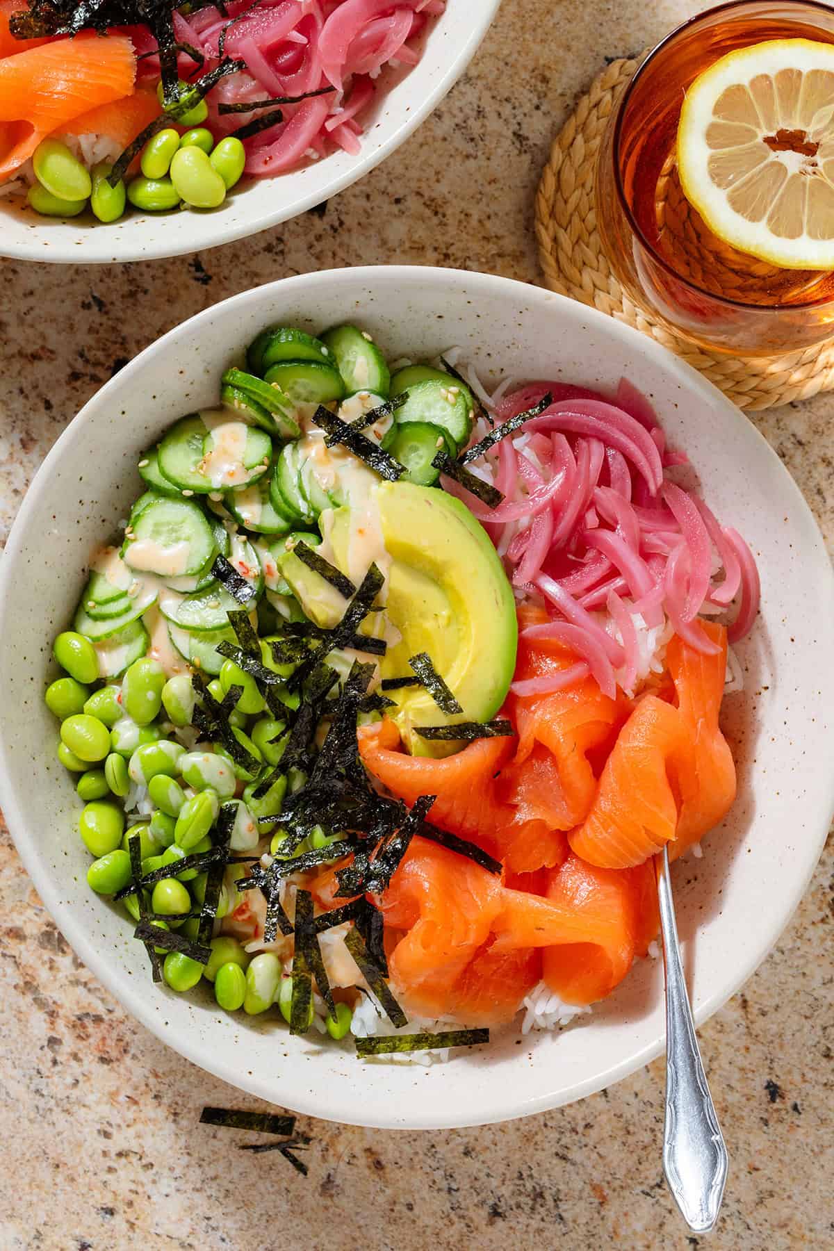 Smoked salmon rice bowl with edamame, cucumber, avocado, pickled red onion, strips of nori, and spicy mayo.