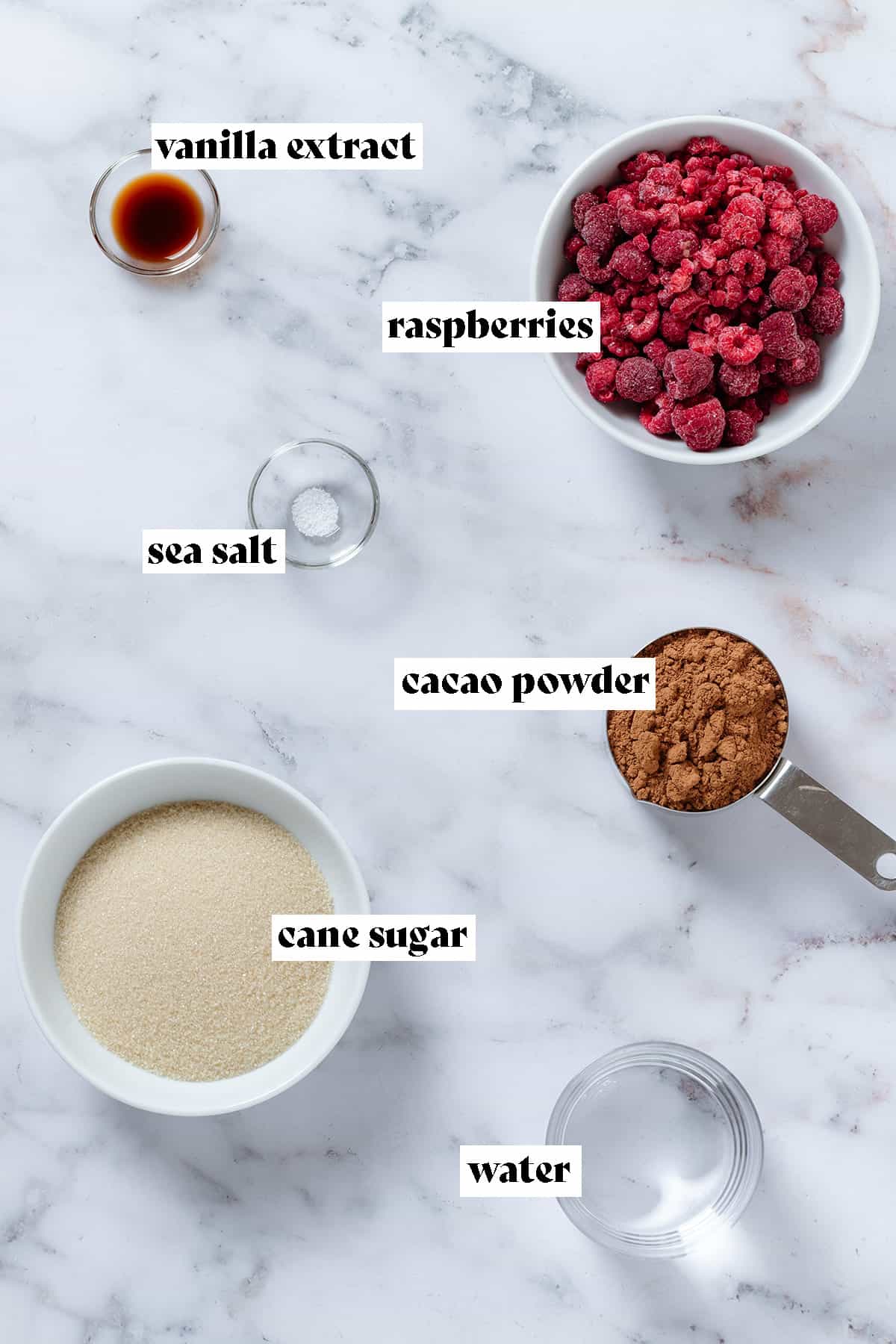 Ingredients like raspberries, cane sugar, cacao powder, vanilla extract, water, and salt in small bowls with text overlay.
