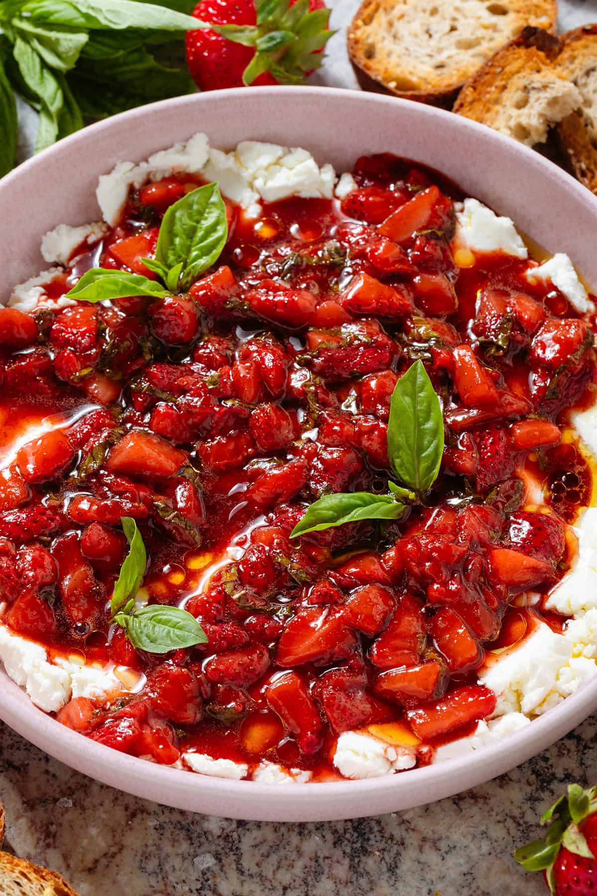 A bowl of soft goat cheese topped with sauteed balsamic strawberries and fresh basil.