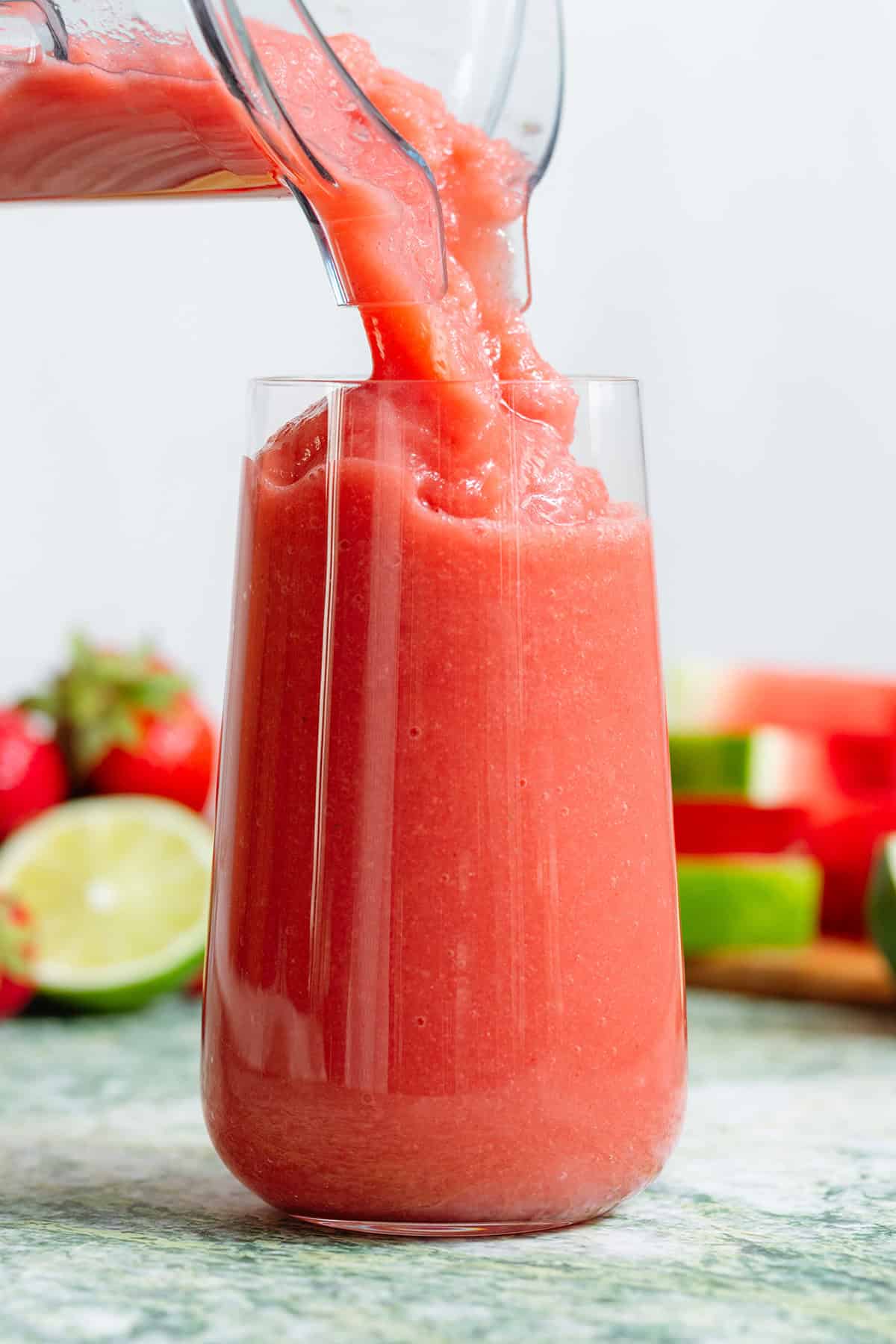 Thick watermelon smoothie being poured into a tall glass.