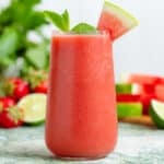 Watermelon smoothie in a tall glass garnished with a wedge of watermelon and fresh mint.