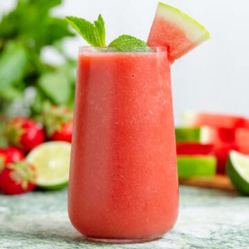 Watermelon smoothie in a tall glass garnished with a wedge of watermelon and fresh mint.