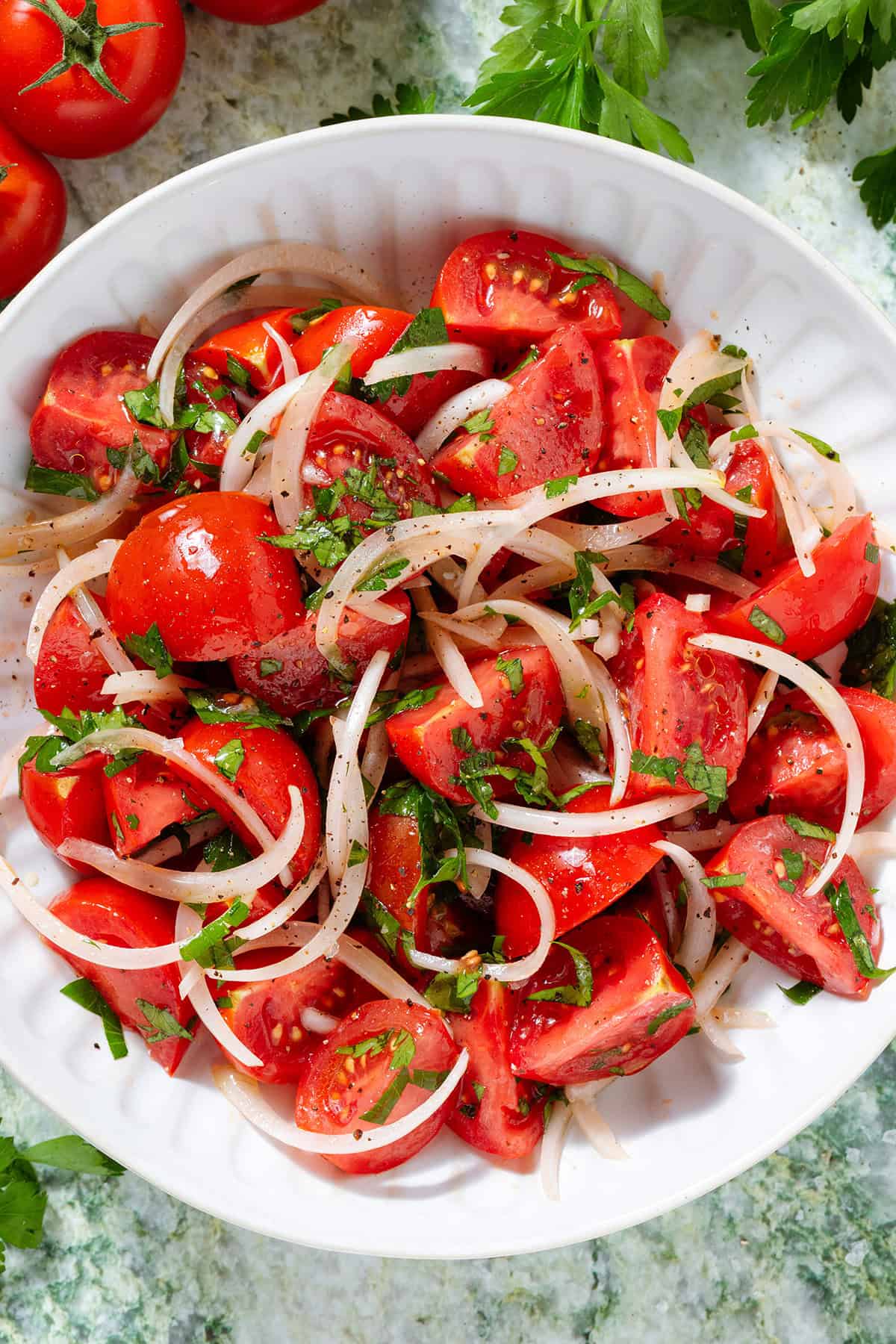 Tomato and onion salad with parsley in a white bowl seasoned with black pepper.