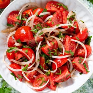 Tomato and onion salad with parsley in a white bowl seasoned with black pepper.