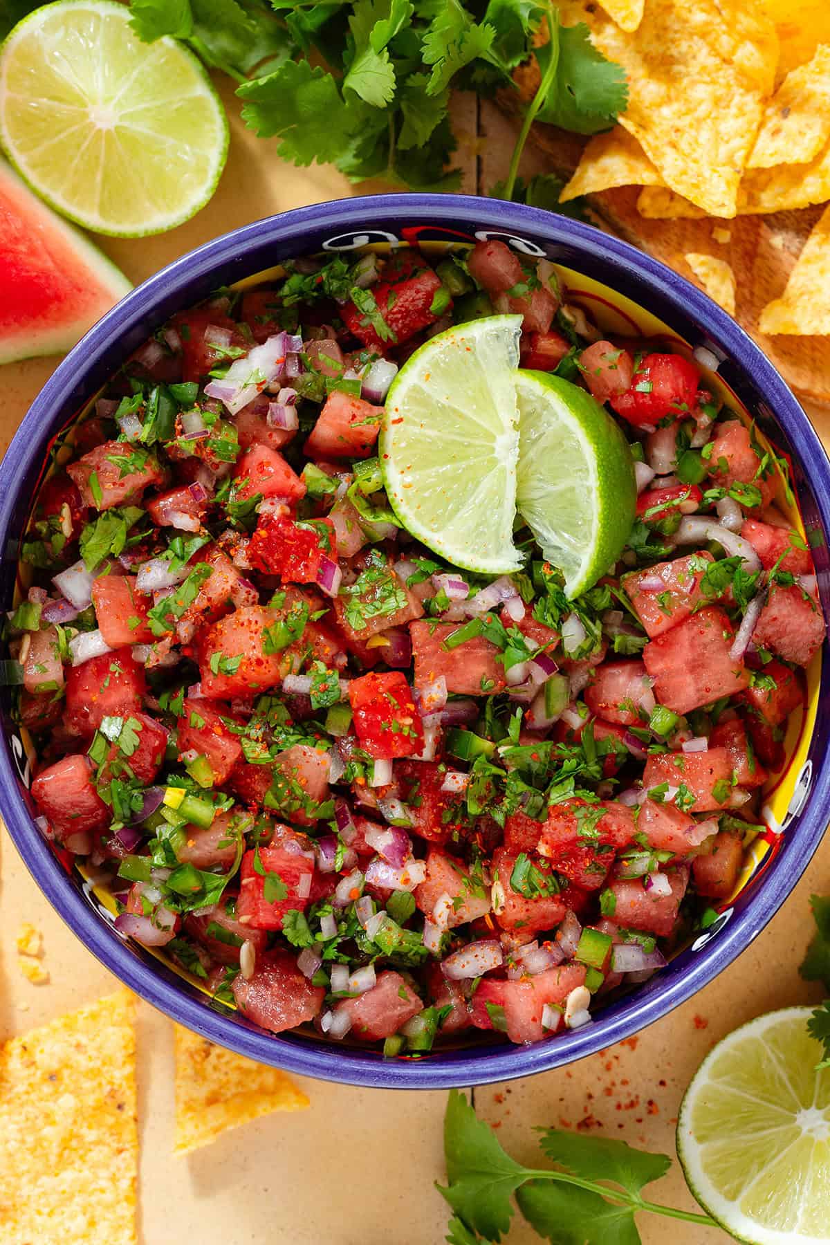 Fresh watermelon salsa in a colorful bowl with a blue rim garnished with two lemon wedges.