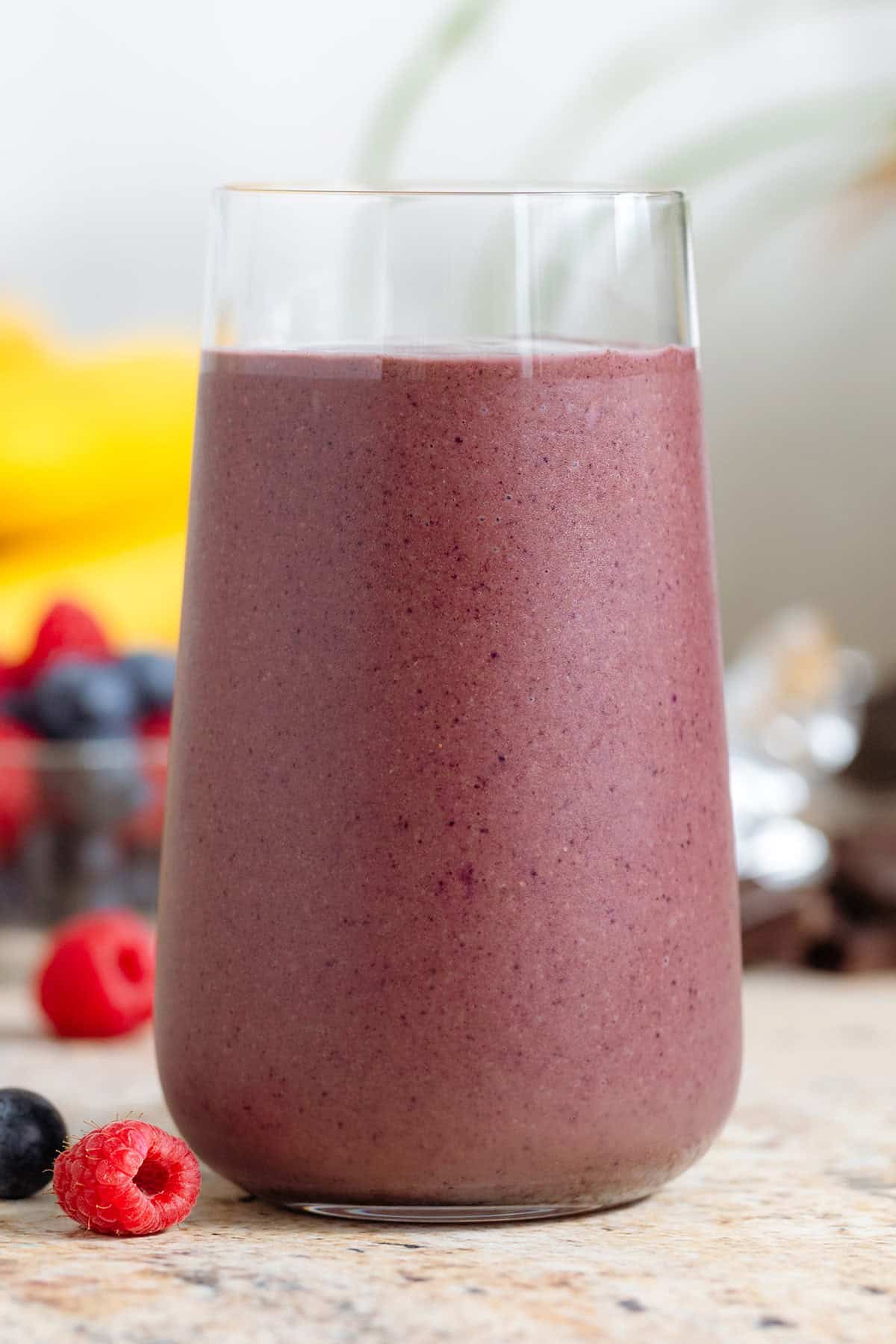 A purple chocolate acai smoothie in a tall glass with berries in the background.