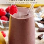 A purple chocolate acai smoothie in a tall glass with a glass straw garnished with a fresh raspberry on the rim with more berries in the background.