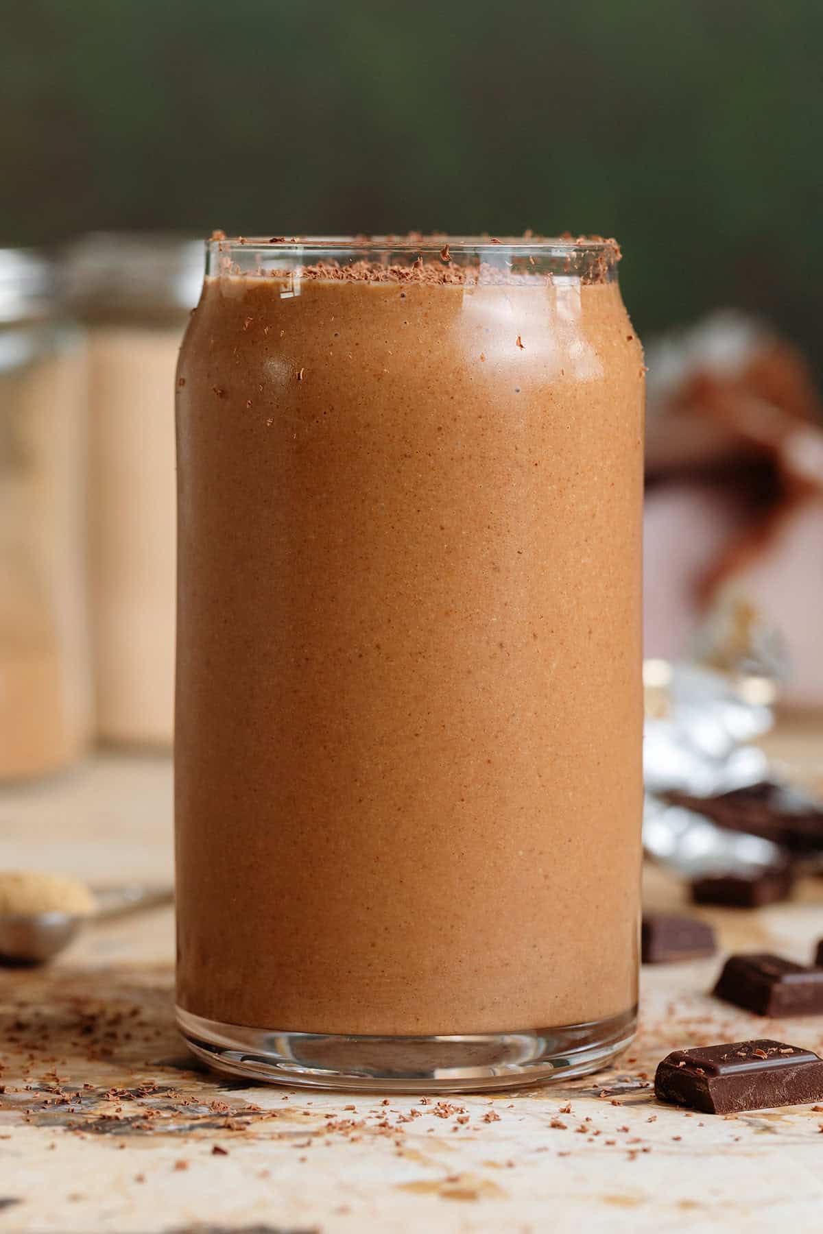 Creamy chocolate smoothie in a glass shaped like a soda can with a glass straw and garnished with grated chocolate.