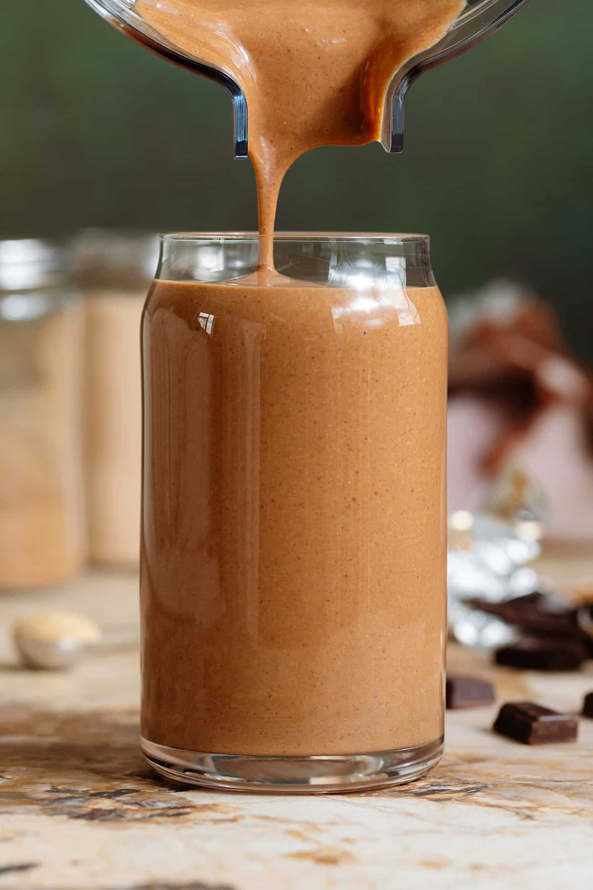 Creamy chocolate smoothie being poured into a tall glass shaped like a soda can from a blender container.