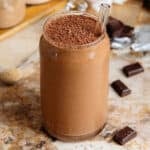 Creamy chocolate smoothie in a glass shaped like a soda can with a glass straw and garnished with grated chocolate.
