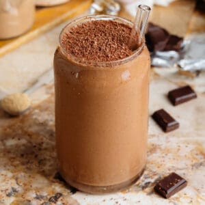 Creamy chocolate smoothie in a glass shaped like a soda can with a glass straw and garnished with grated chocolate.