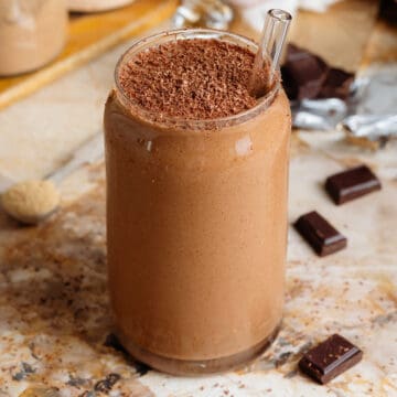 Creamy chocolate smoothie in a glass shaped like a soda can with a glass straw and garnished with grated chocolate.