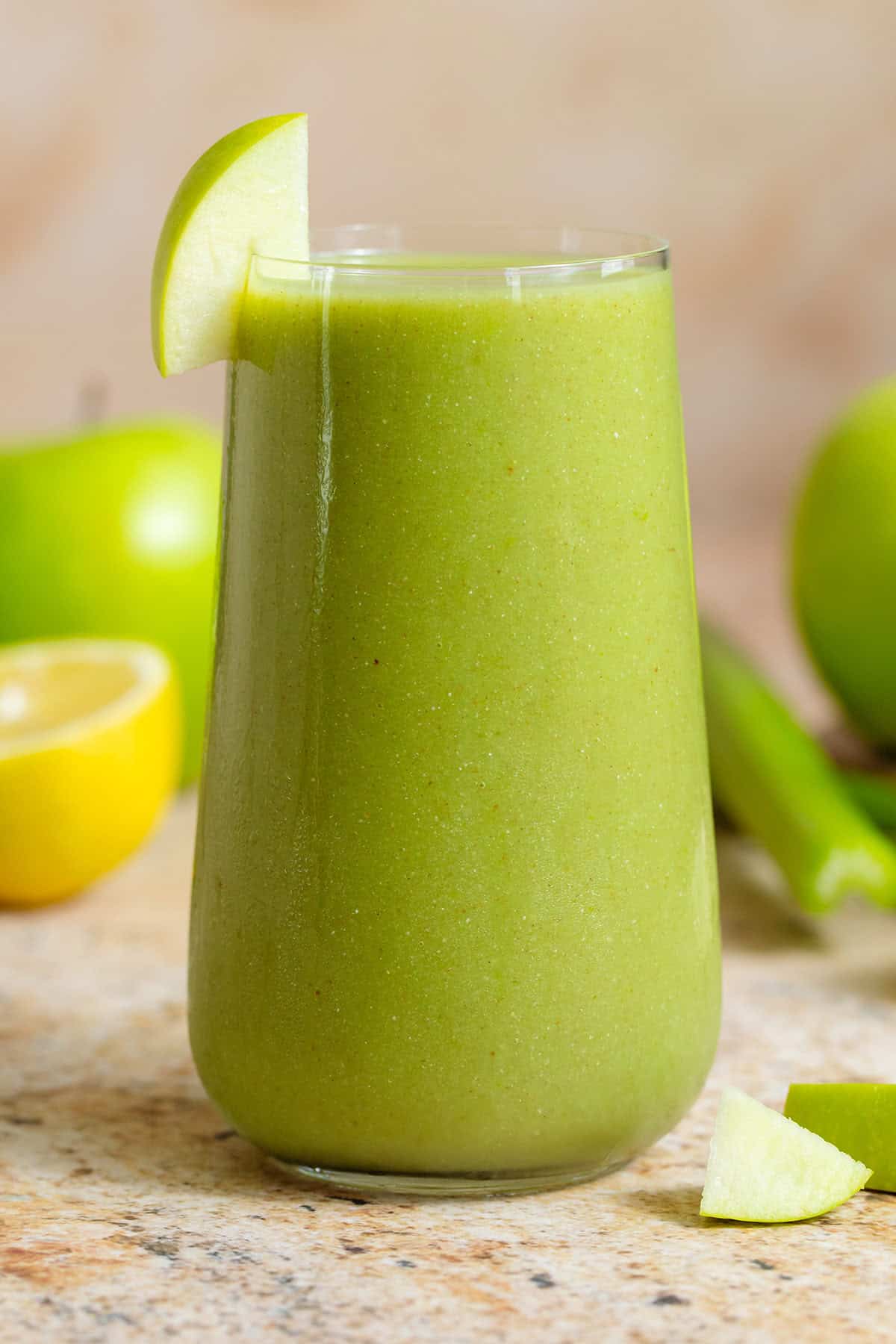 Bright green smoothie in a tall glass garnished with a slice of a green apple.