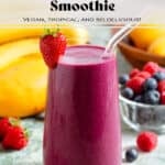 A tall glass with bright purple maqui berry smoothie and a glass straw garnished with a strawberry.
